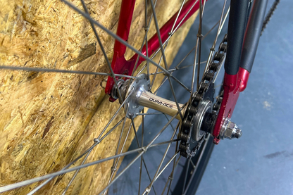 Close-up of a bicycle wheel with red frame and 'Dura-Ace' gear system against a textured wall.