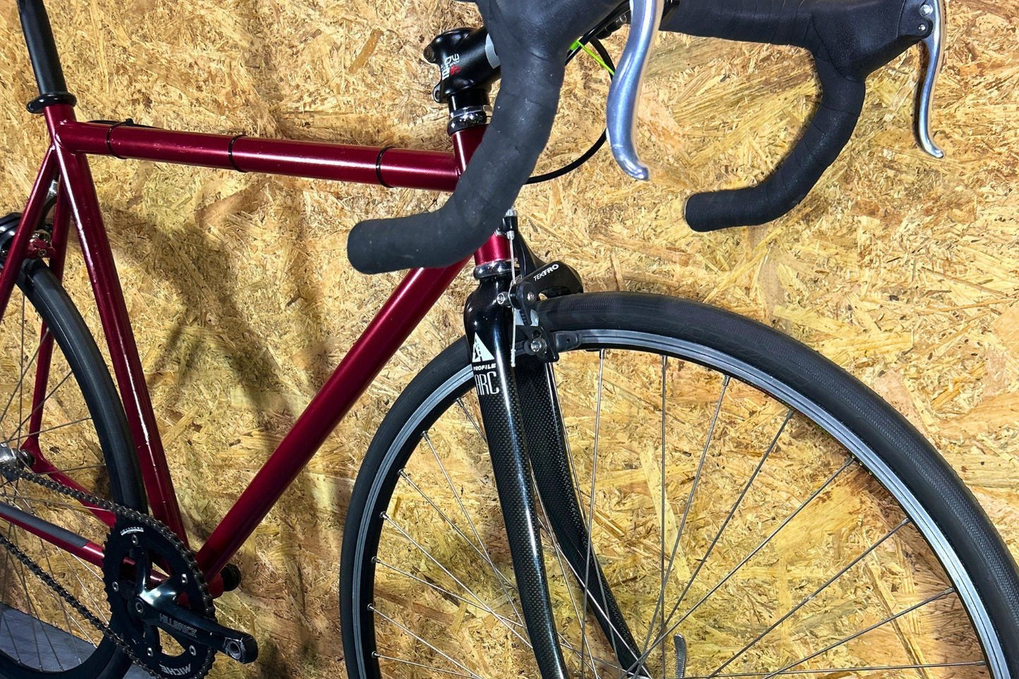 Red bicycle with black handlebars and tires against a wooden background