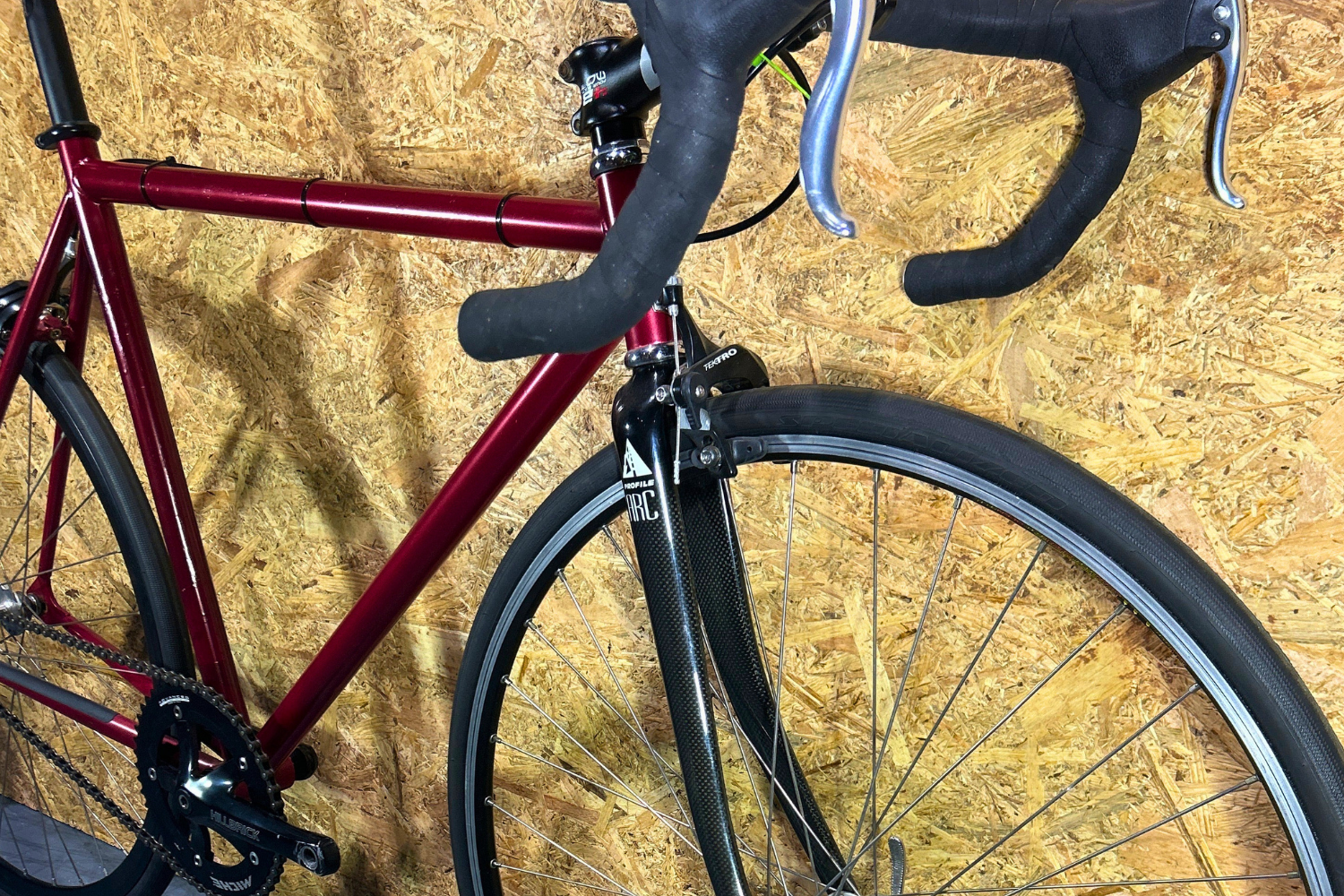 Red bicycle with black handlebars and tires against a wooden background